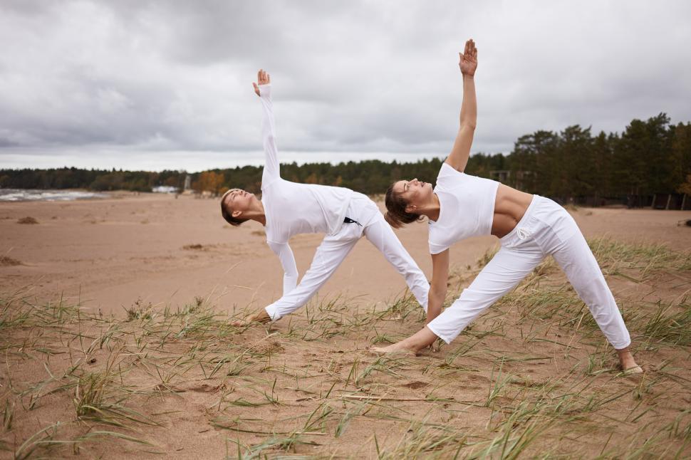Free Image of People, fitness, sport, friendship, family and lifestyle concept. Professional female yoga instructor and her teenage son both in white clothes, standing barefooted on sand, doing Utthita Trikonasana 
