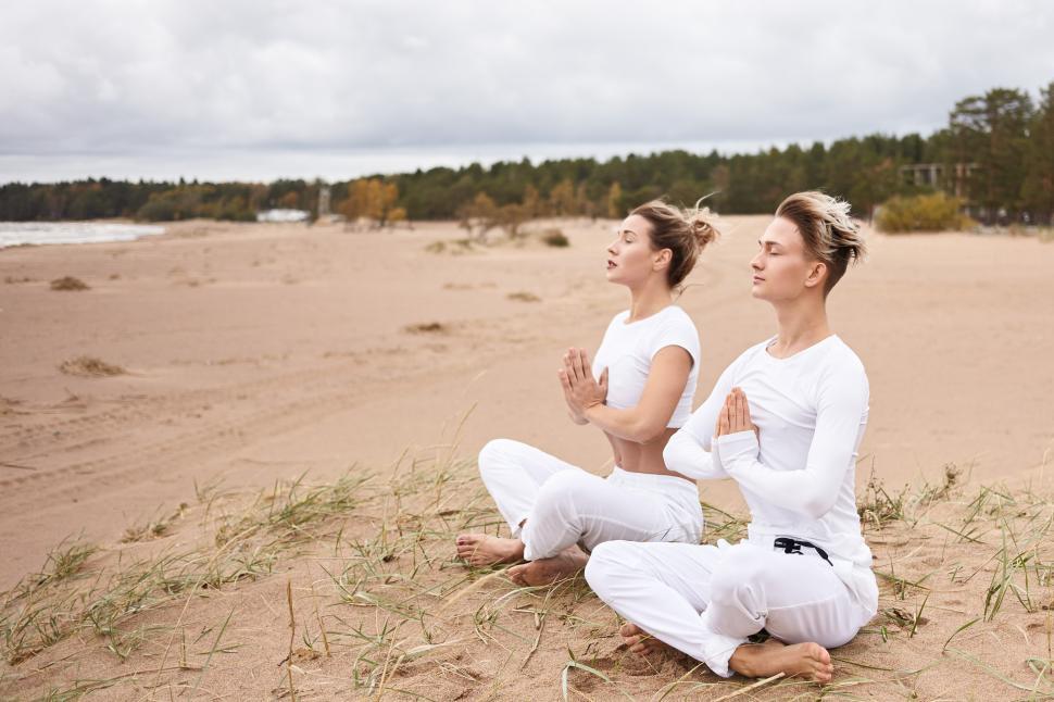 Free Image of Yoga, zen, enlightenment, reacreation, meditation and concentration concept. Young male and female wearing white clothes meditating with eyes closed, making namaste gesture, sitting in lotus pose 