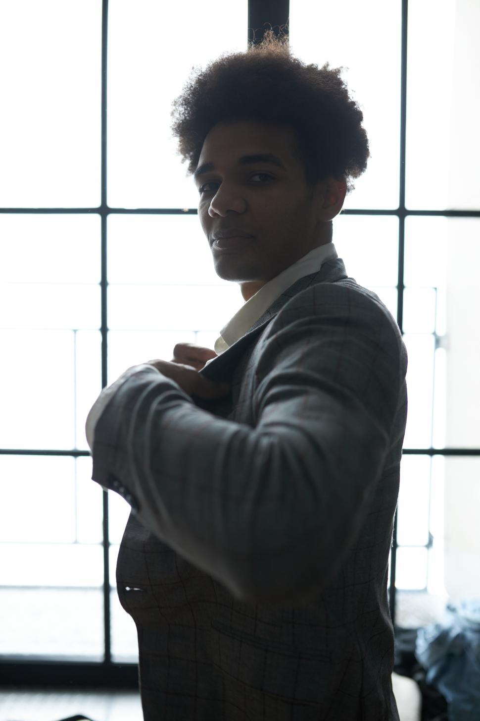 Free Image of Vertical side view image of elegant african american businessman getting ready for business meeting, putting on and buttoning his jacket standing against big window, looking at camera 
