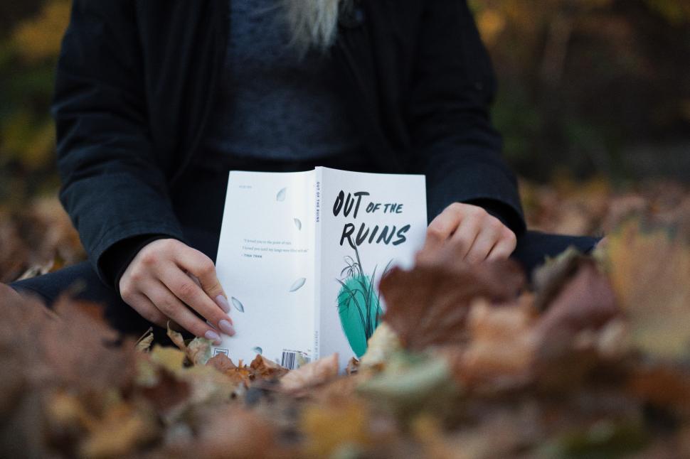 Free Image of Person reading book  Out of the Ruins  in leaves. 