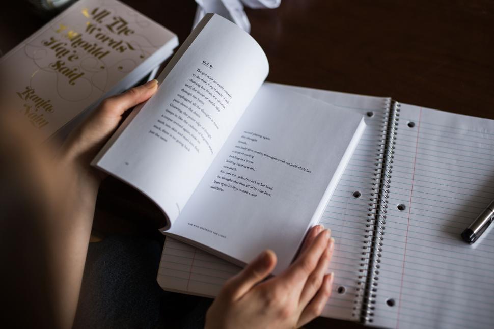 Free Image of Person reading with open book and notebook nearby. 