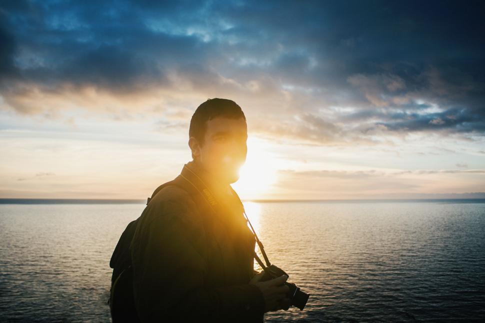 Free Image of Silhouetted figure with camera at sunset by the sea 