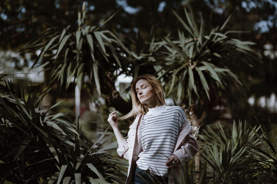 Free Image of Woman in striped shirt posing in lush tropical setting. 
