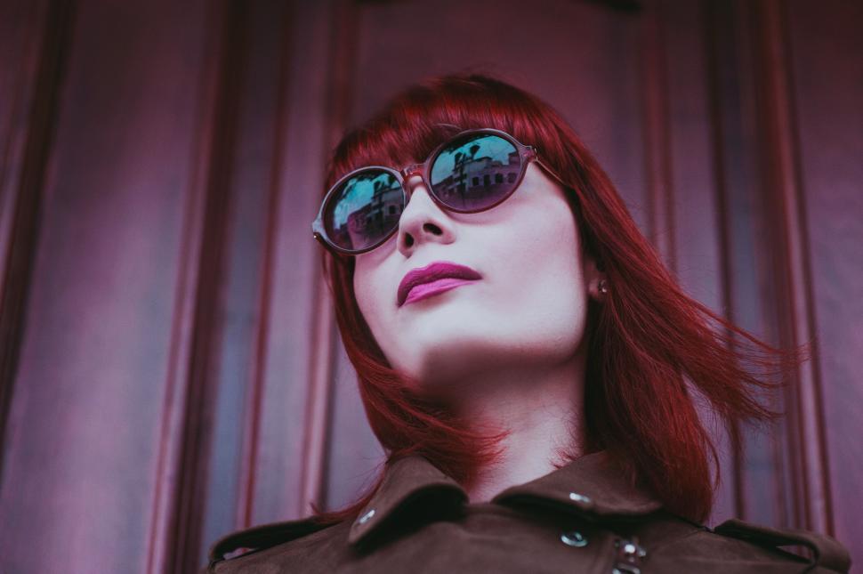 Free Image of Red-haired woman wearing glasses with purple backdrop. 