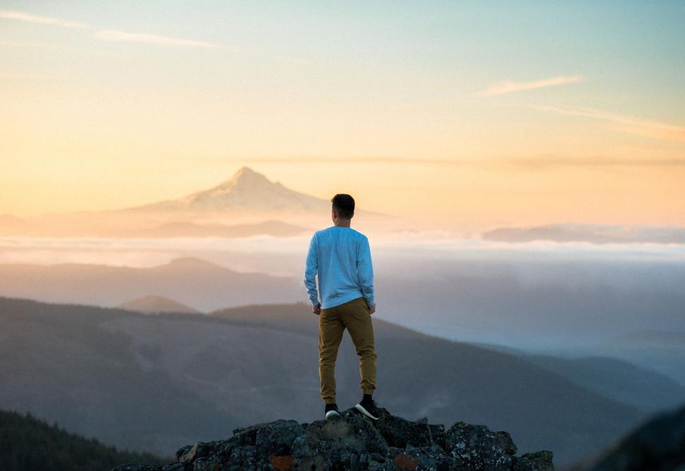 Free Image of Man standing on cliff with mountain view during sunrise 