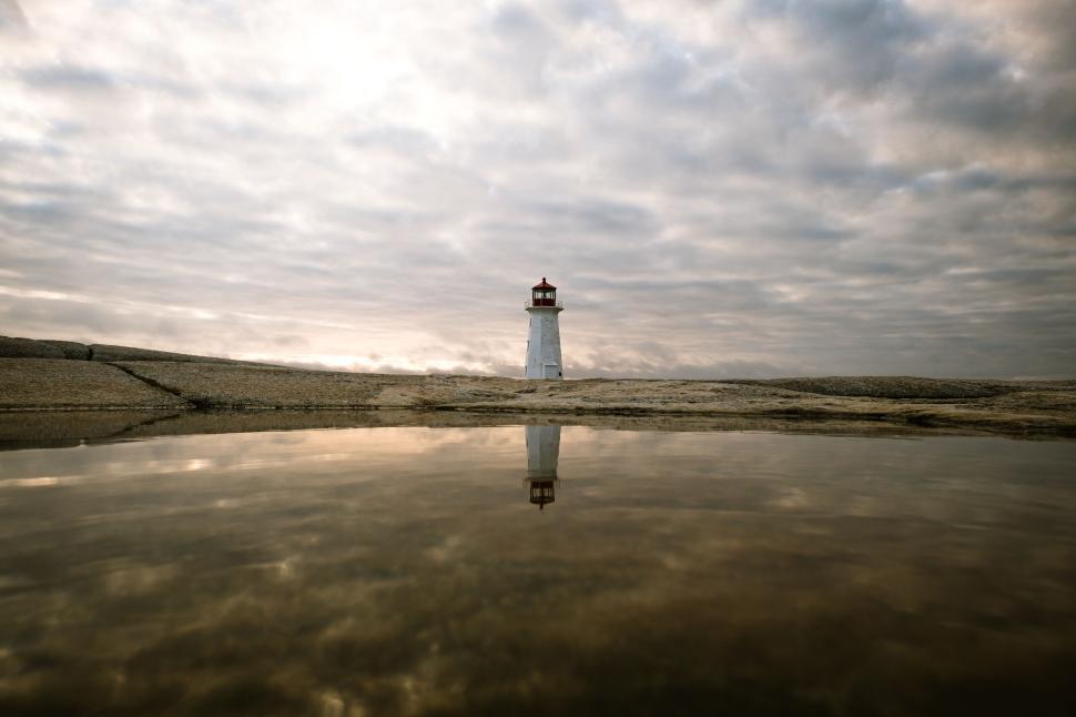 Free Image of Lighthouse reflecting on calm water under cloudy sky 