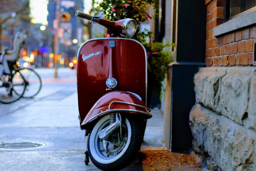 Free Image of Retro maroon scooter parked beside a brick building 