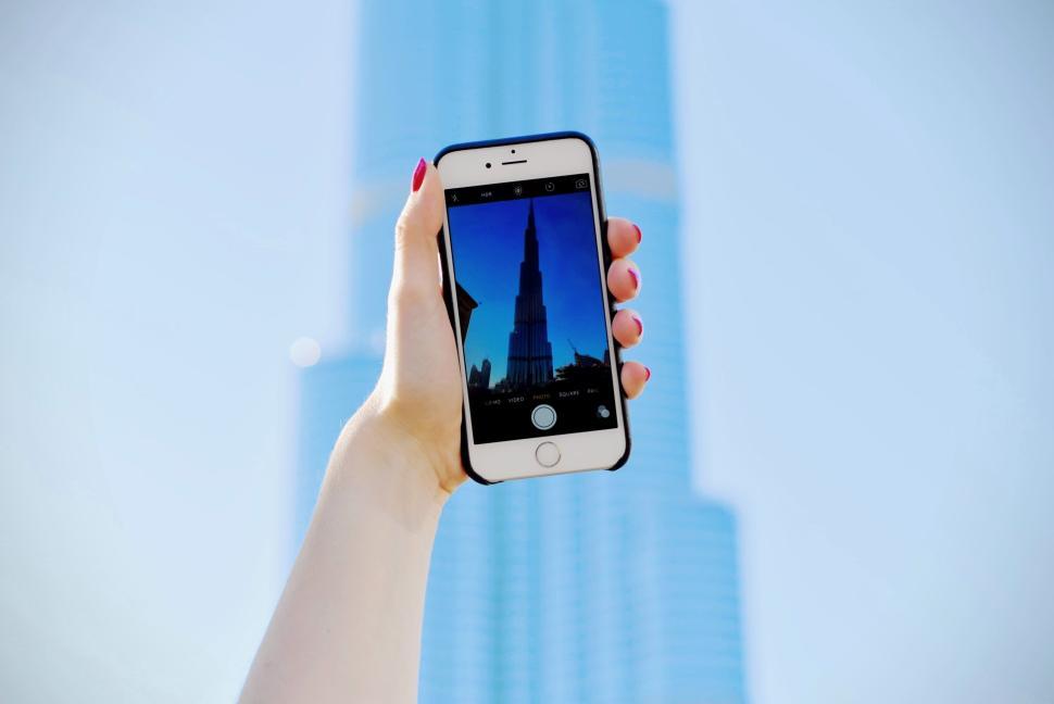 Free Image of Hand holding phone capturing a tall glass skyscraper image. 