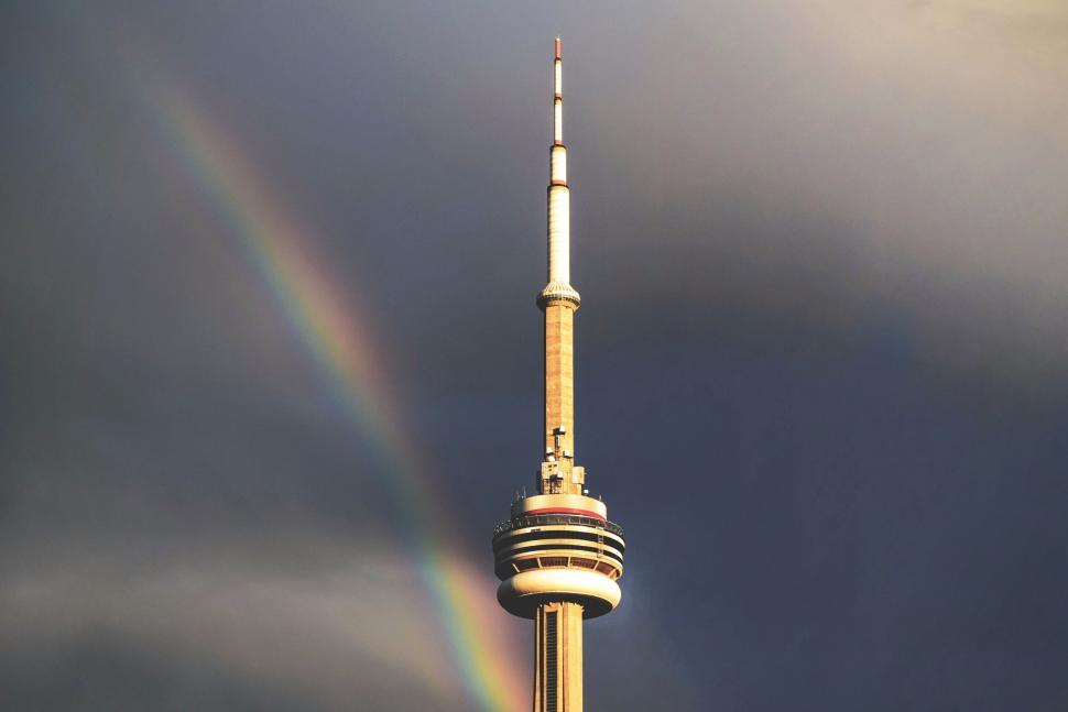 Free Image of Tower with rainbow arcing through cloudy sky background 