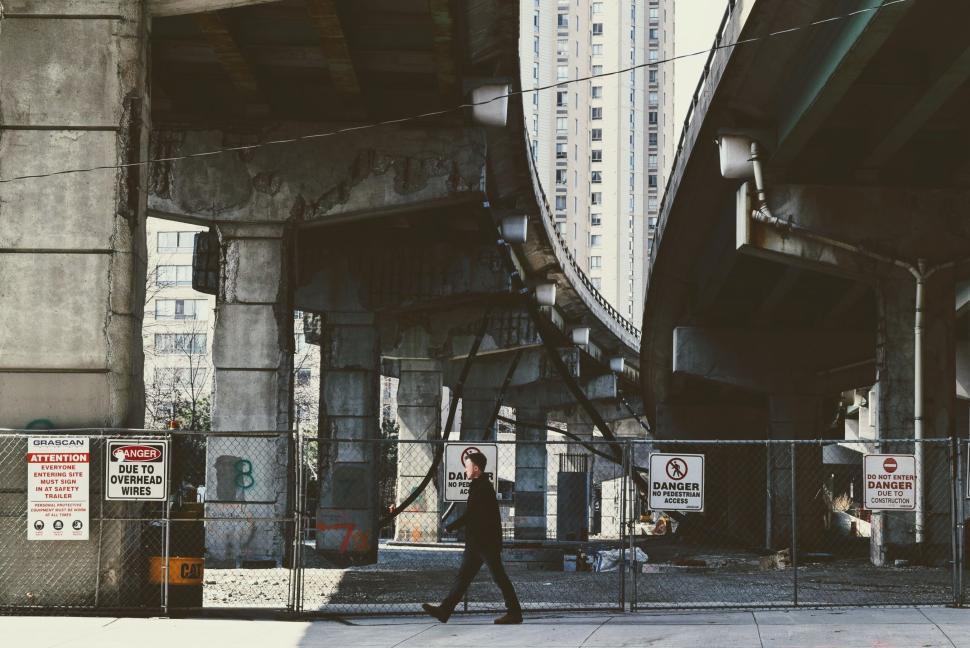 Free Image of Man walking under a bridge in an urban construction site 