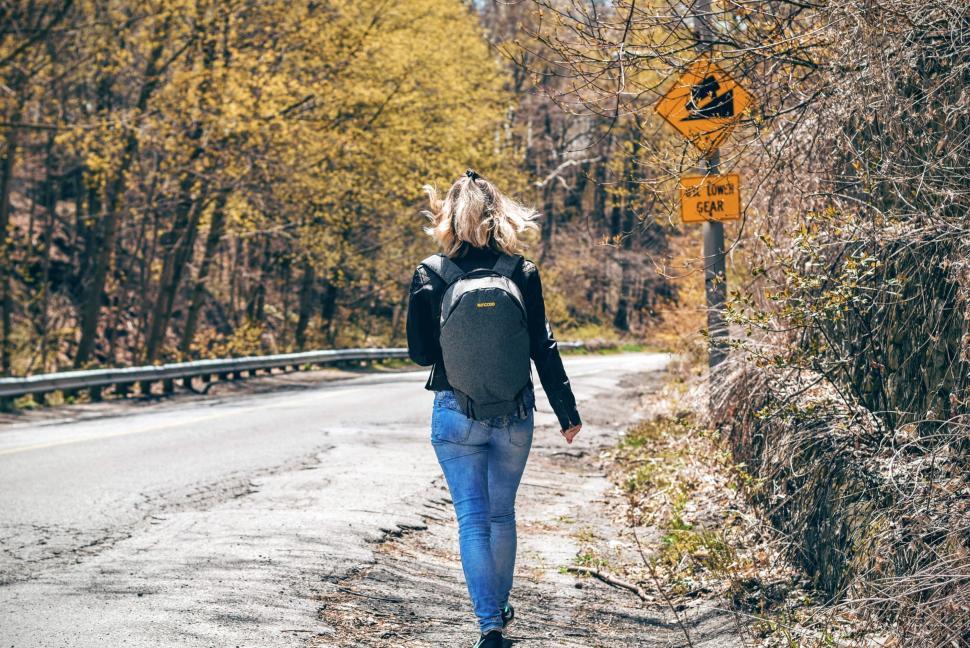 Free Image of Solo hiker walking along empty roadside with forest view. 