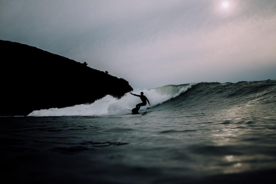 Free Image of Surfer riding a wave near rocky shore at sunset time 