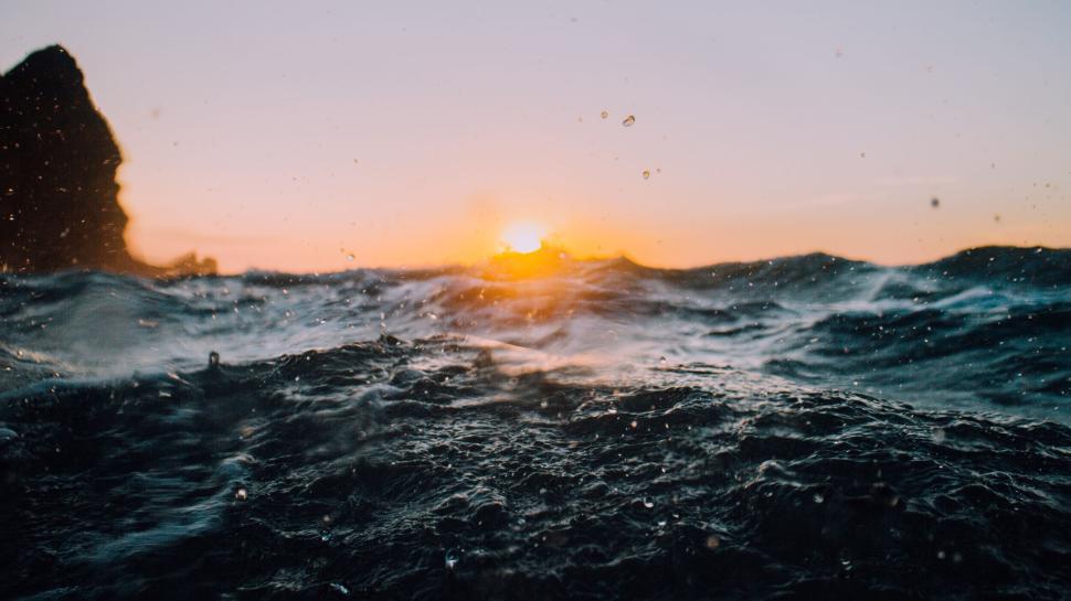 Free Image of Sunset over the ocean with waves in the foreground 