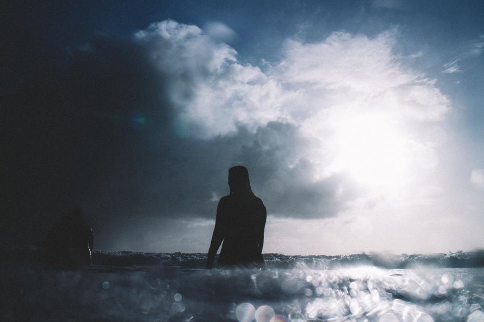 Free Image of Silhouetted person in ocean at sunset with clouds 