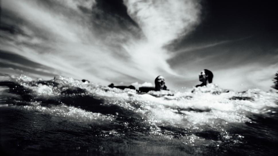 Free Image of Two people swimming in ocean with dynamic sky overhead. 