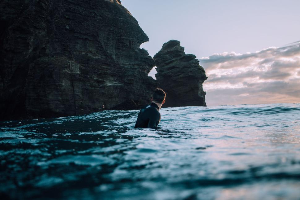 Free Image of A solitary person swimming near coastal rock formation. 