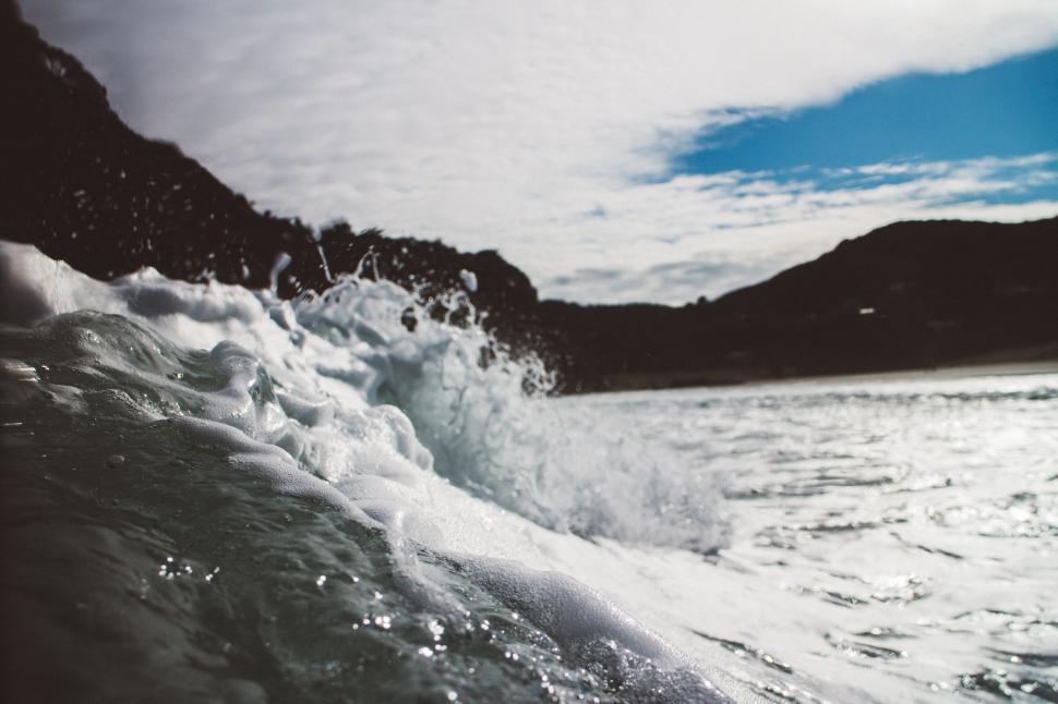Free Image of Ocean wave crashing near peaceful, mountainous coastline. 
