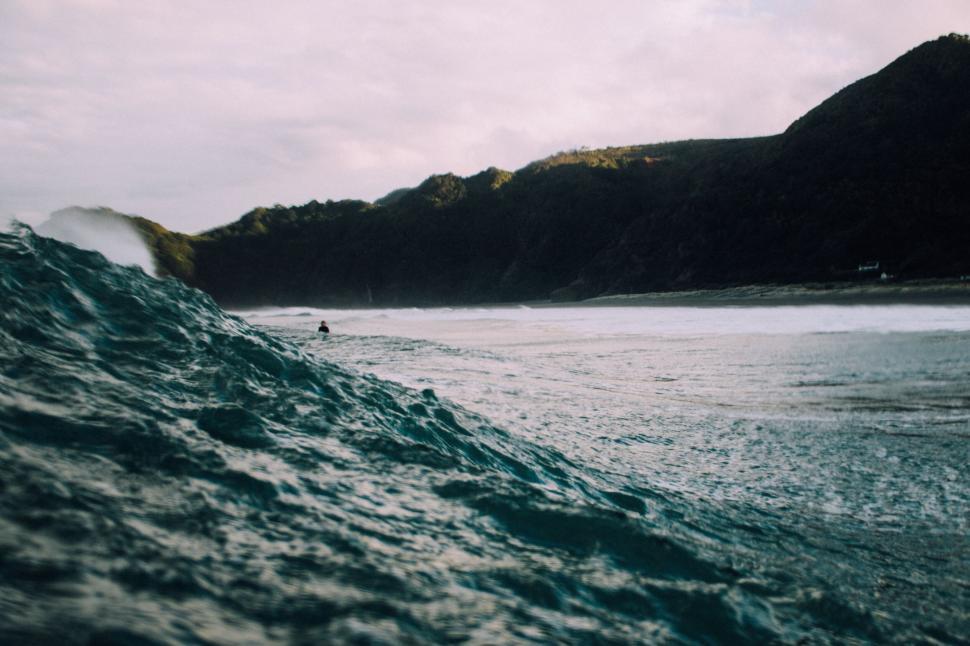 Free Image of Large ocean wave with distant surfer under cloudy sky 