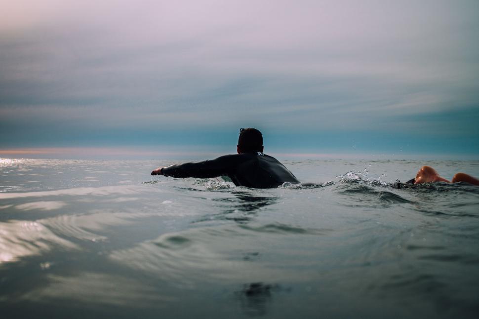 Free Image of Surfer paddling in calm ocean water during twilight 