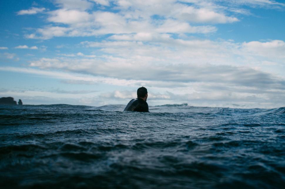Free Image of Person waiting in ocean with surfboard under blue sky 