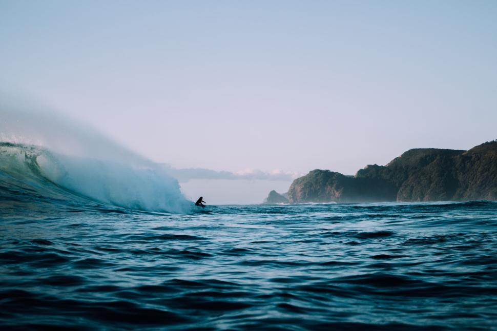 Free Image of Surfer riding ocean wave near rocky coastline at dusk 