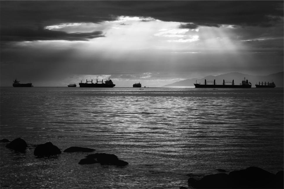 Free Image of Multiple cargo ships on calm sea with sun rays breaking clouds. 