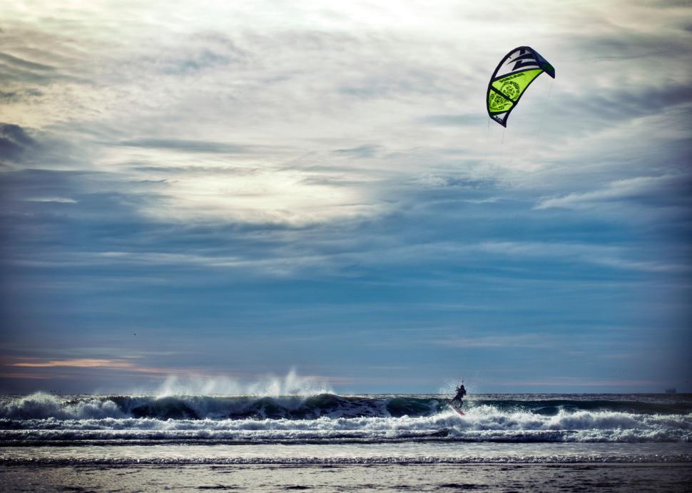 Free Image of Kite surfer riding waves under a cloudy blue sky 
