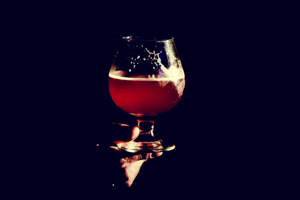 Free Image of Hand holding a glass of craft beer against dark backdrop. 