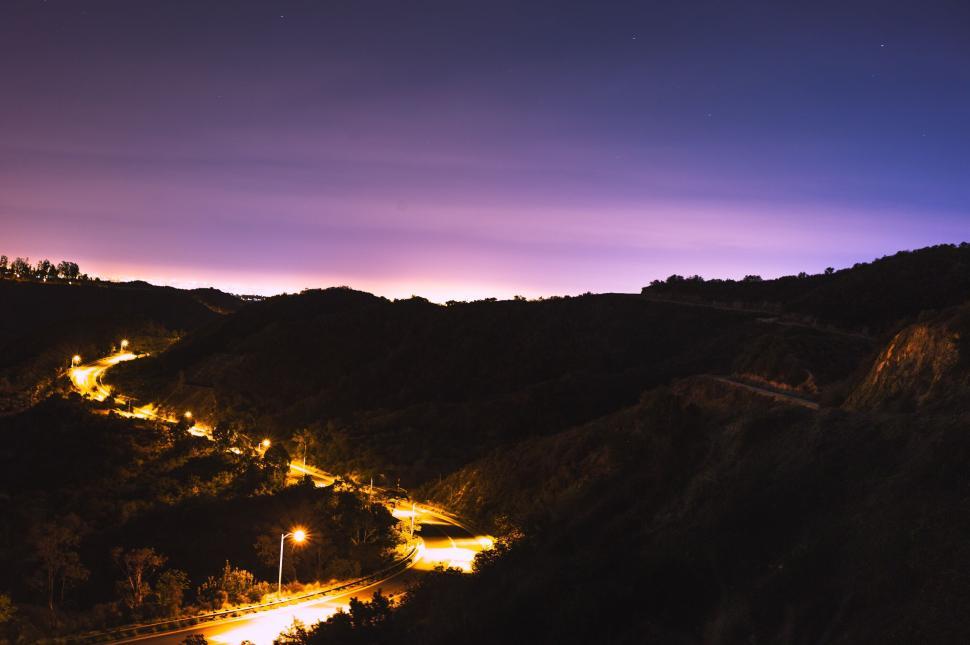 Free Image of Winding road with glowing lights through hills at twilight 