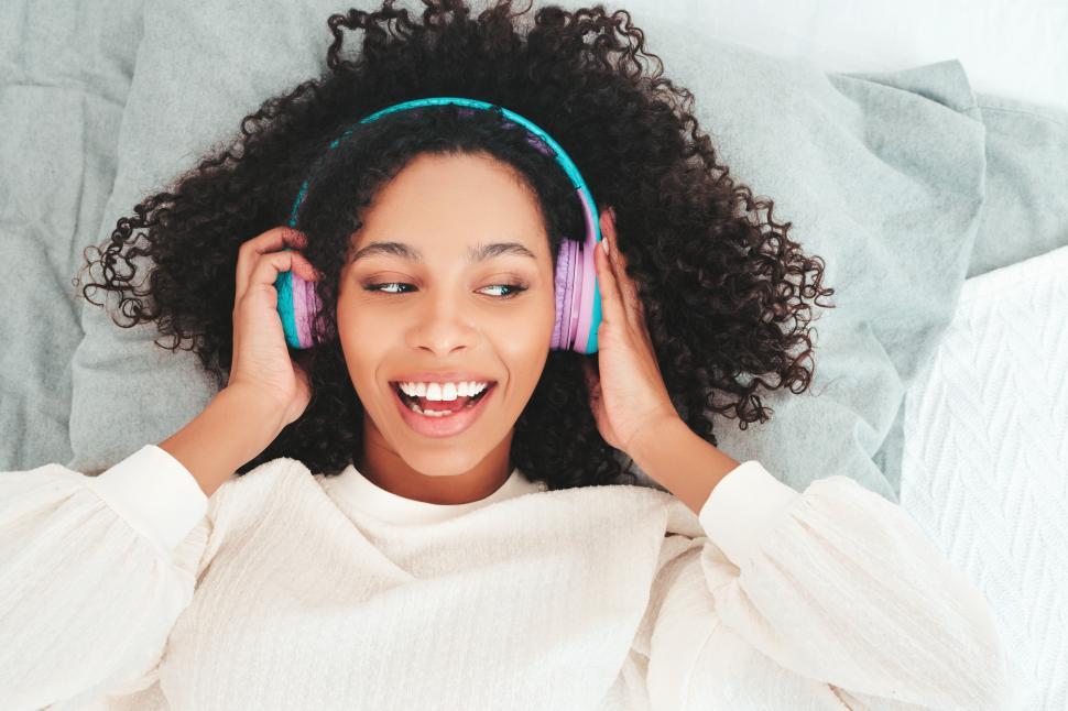 Free Image of Woman enjoying music lying on bed with headphones. 
