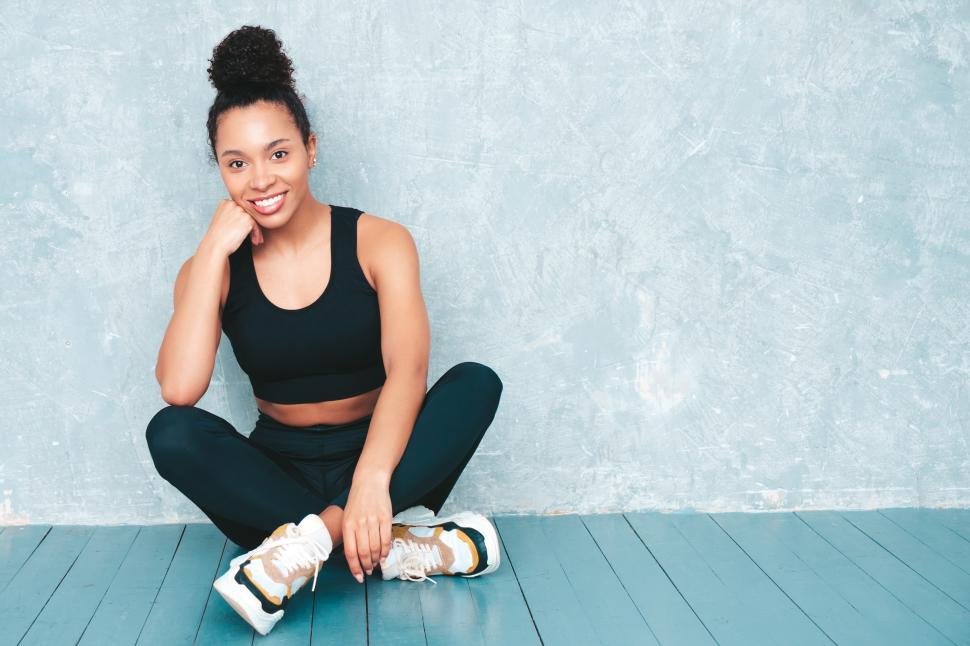 Free Image of Woman sitting on floor smiling in athletic wear 
