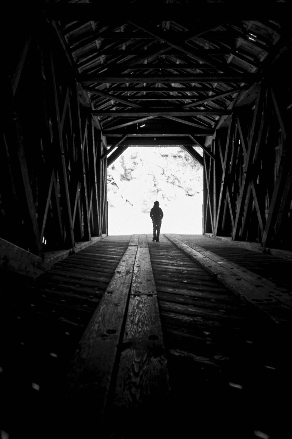 Free Image of Person standing under an old wooden bridge tunnel. 