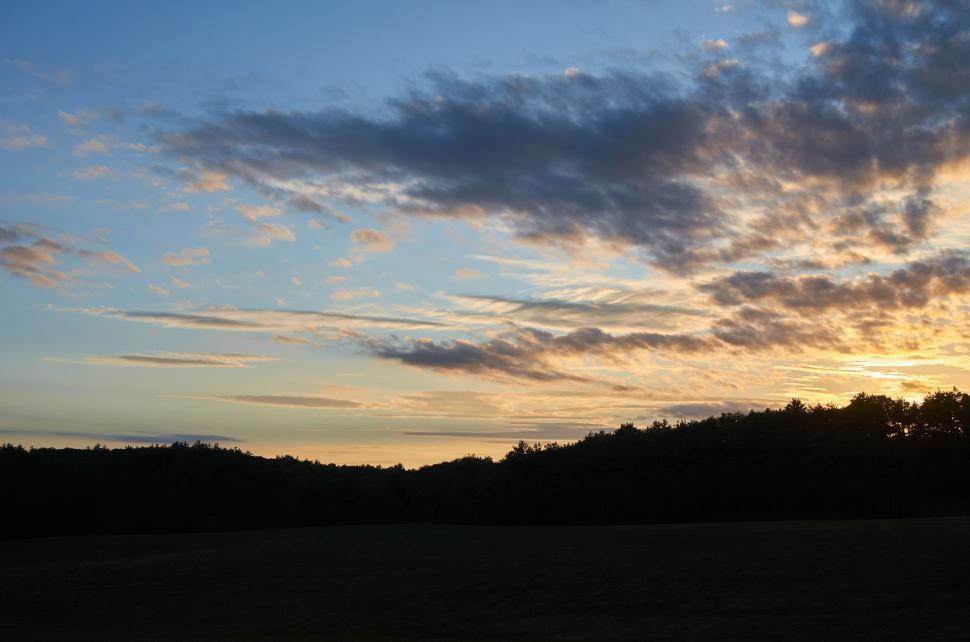 Free Image of Sunset over a field with a cloudy sky backdrop 