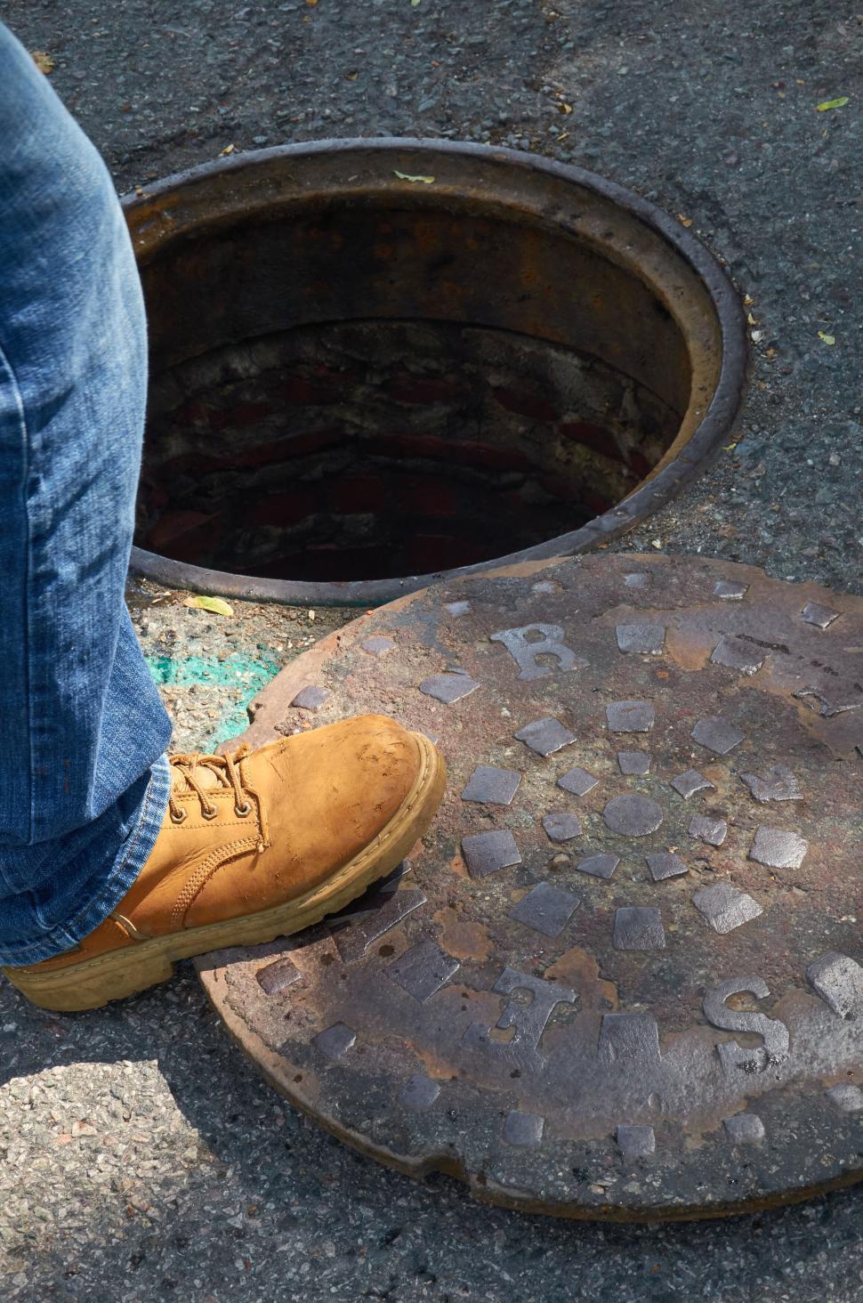 Free Image of Person standing by an open manhole on a paved street. 
