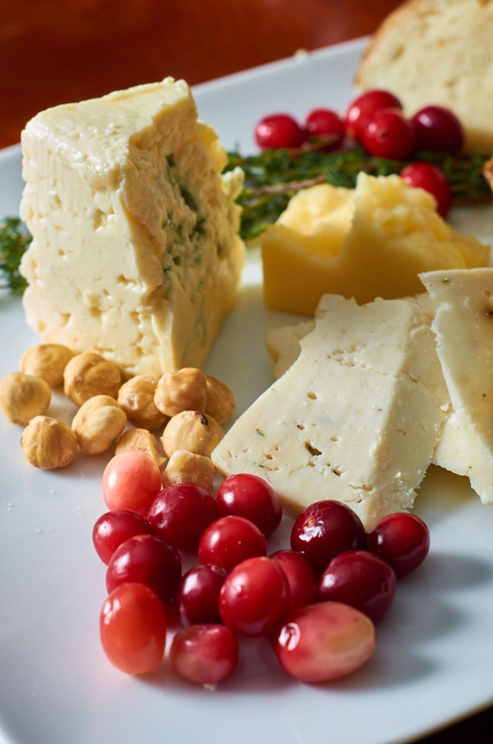 Free Image of Assorted cheeses, nuts, and fruits on a white platter. 