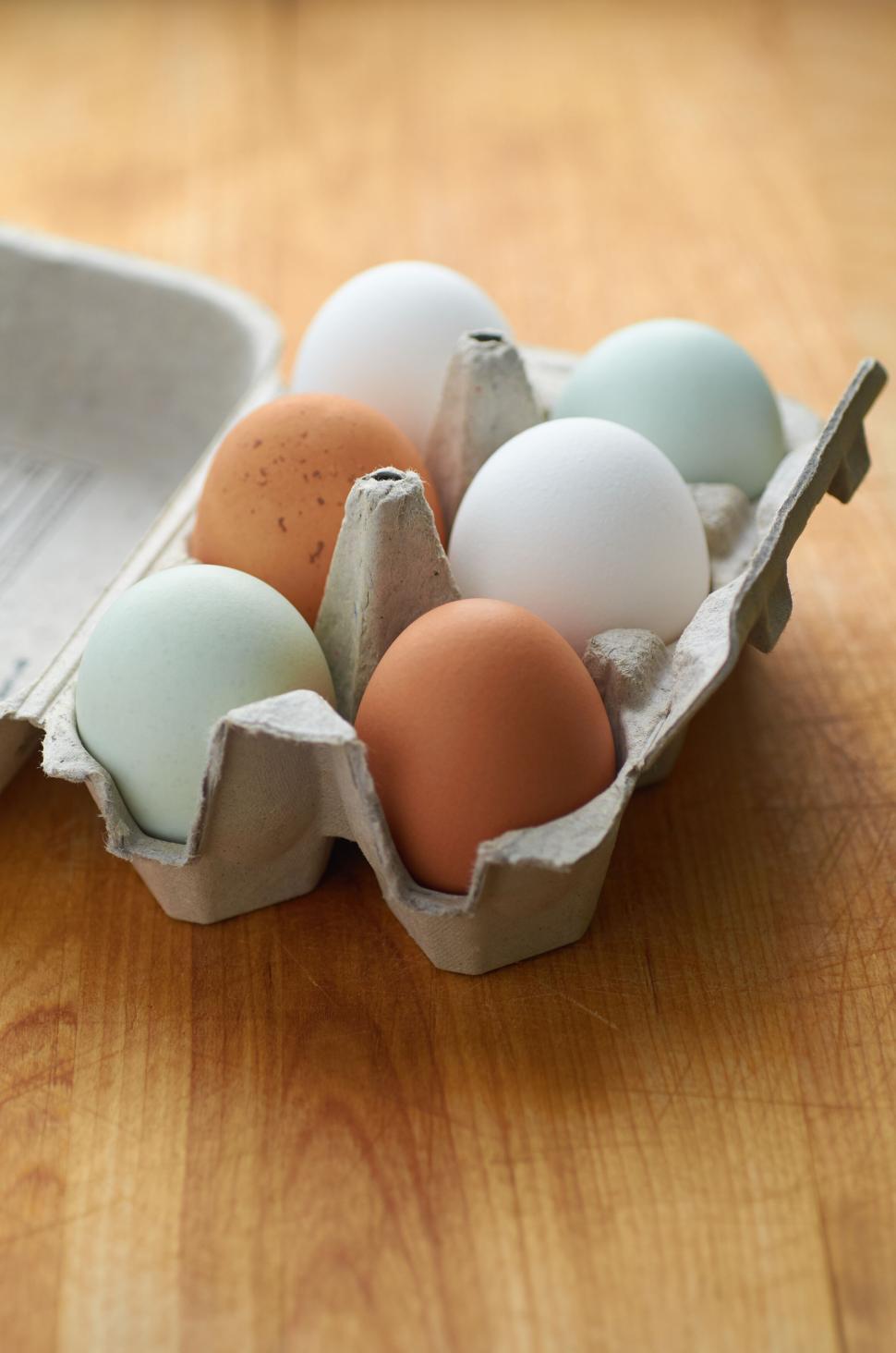 Free Image of A carton of six multi-colored eggs on wooden surface 