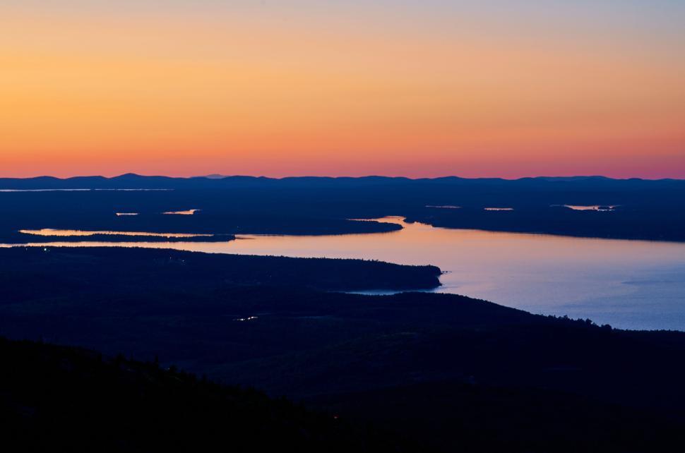 Free Image of Serene sunset over a calm lake with distant mountains 