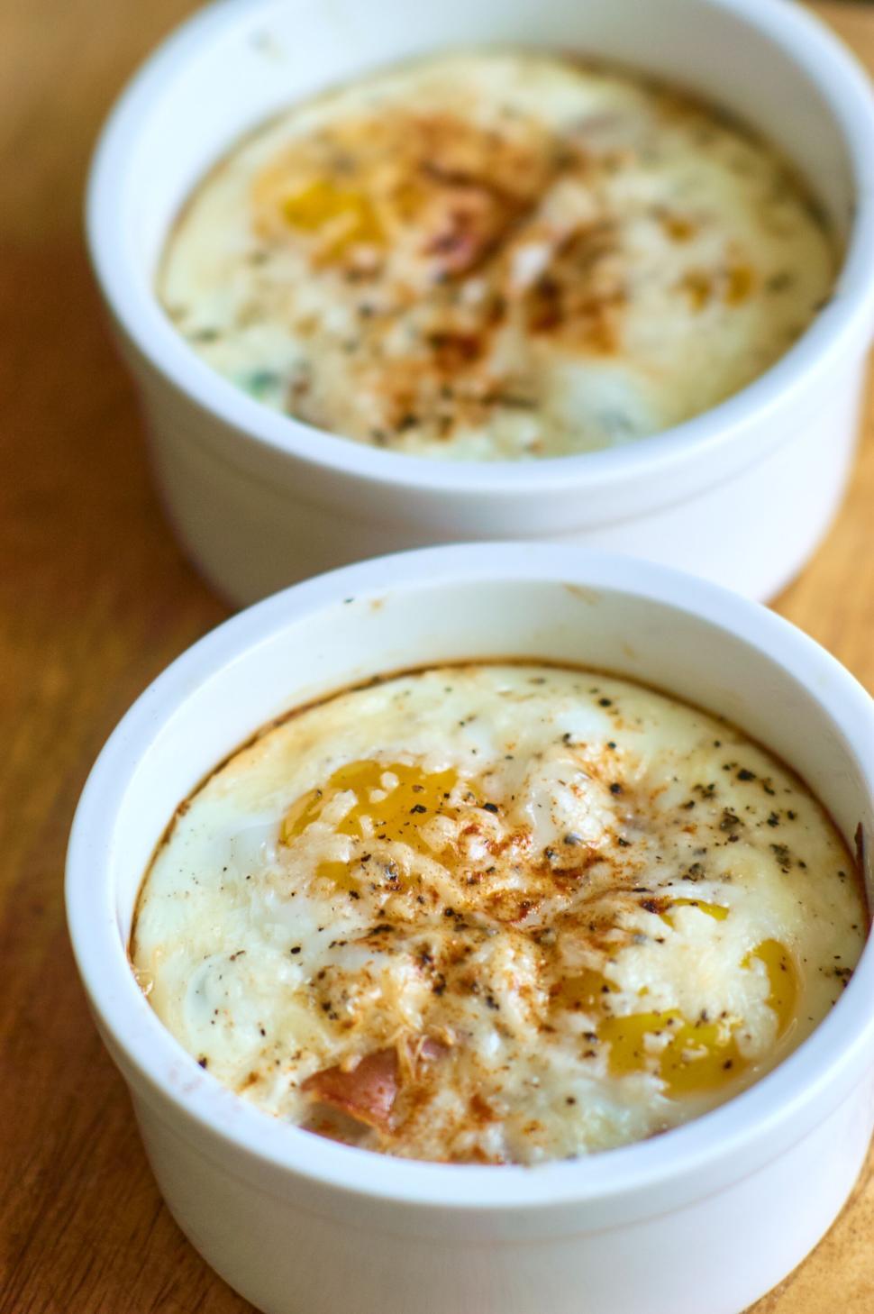 Free Image of Baked eggs in ceramic ramekins with melted cheese on top 