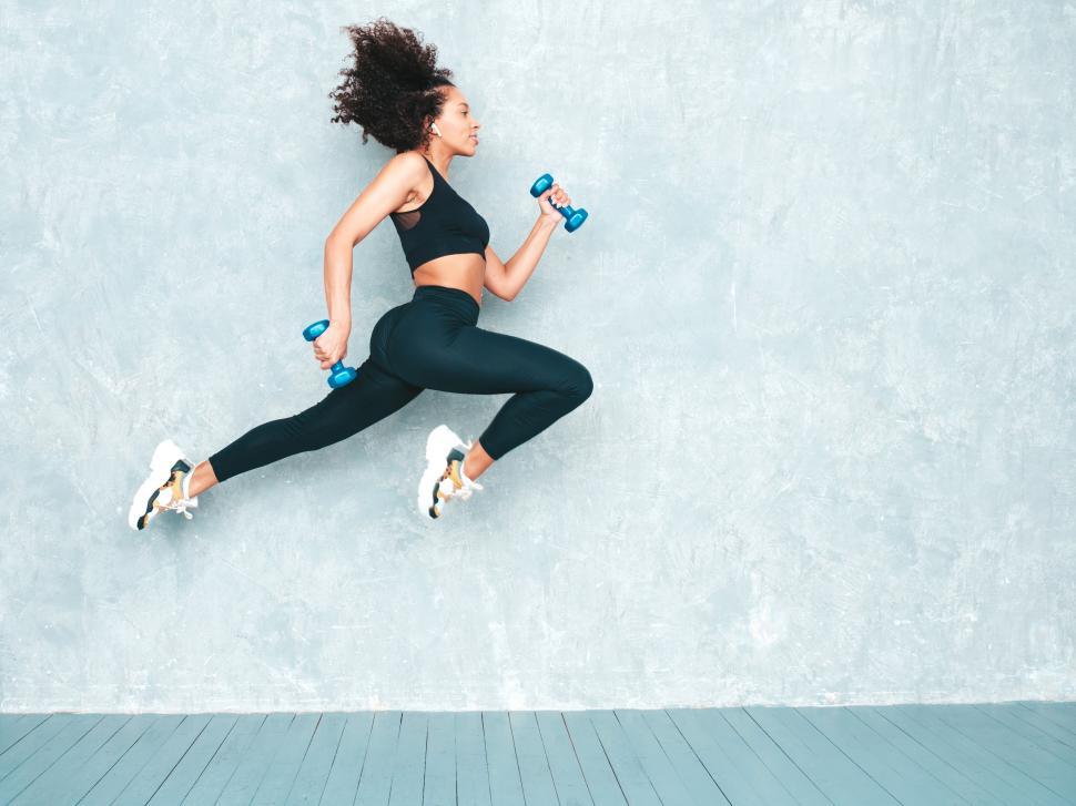 Free Image of Woman mid-leap with dumbbells in workout attire 