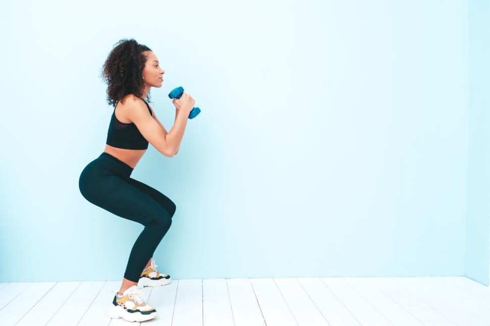 Free Image of Woman squatting with dumbbells in athletic gear 