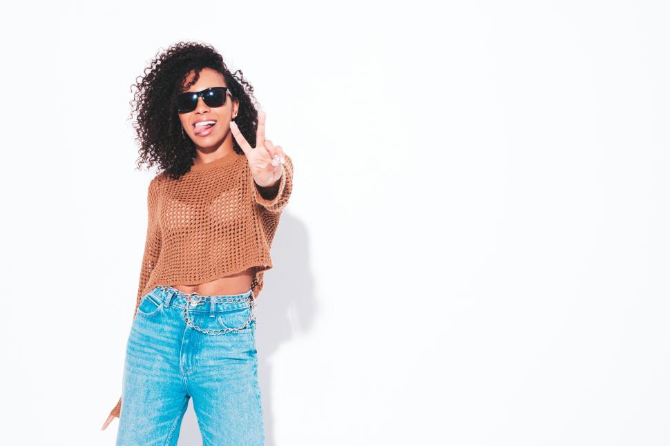 Free Image of Woman in brown sweater and jeans flashing peace sign 