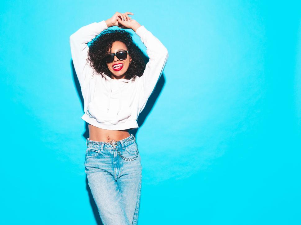 Free Image of Woman in white hoodie posing against blue backdrop. 