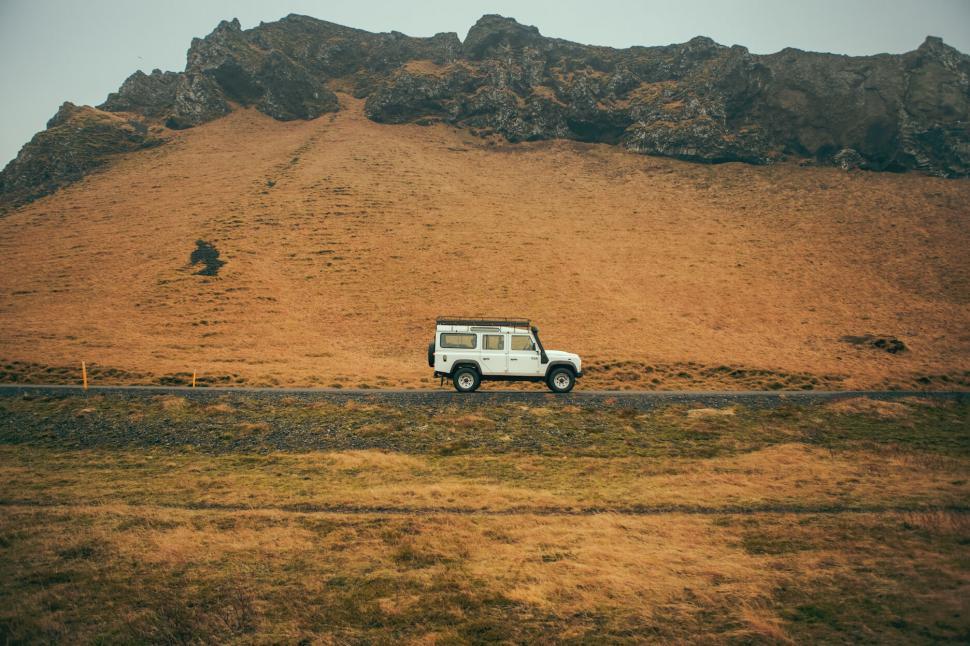 Free Image of White off-road vehicle driving past brown grassy hill 