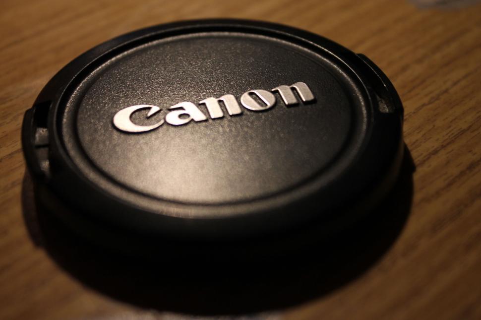 Free Image of Canon camera lens cap resting on a wooden surface. 