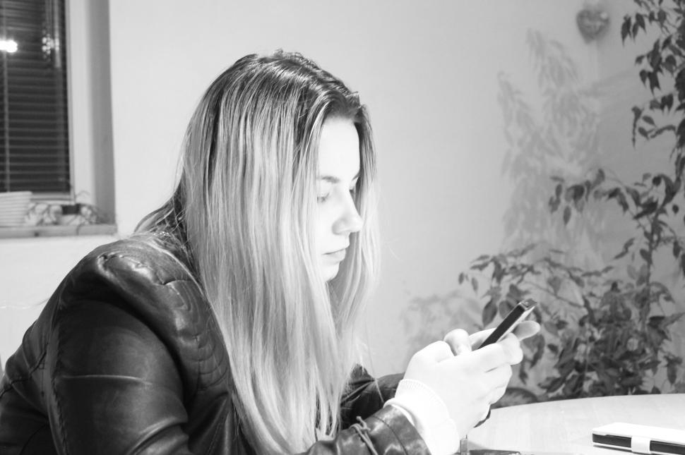 Free Image of Young woman in black jacket focused on smartphone indoors 