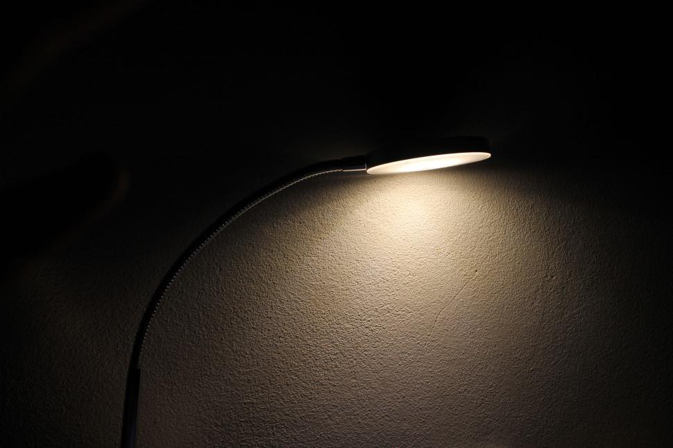 Free Image of Minimalistic desk lamp casting light on a dark wall. 