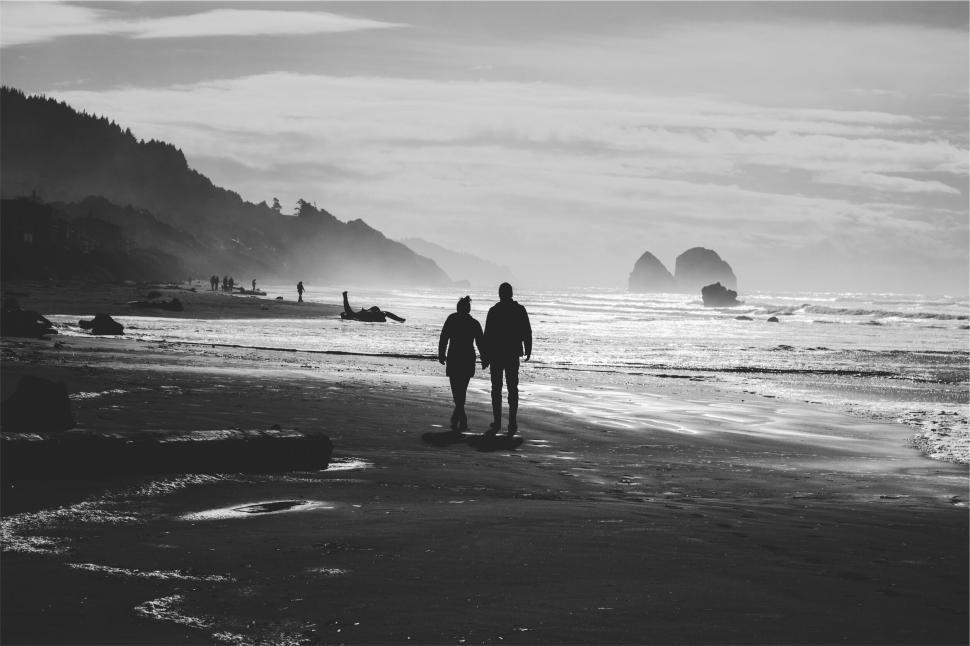 Free Image of Two silhouetted individuals walking along sandy beach. 
