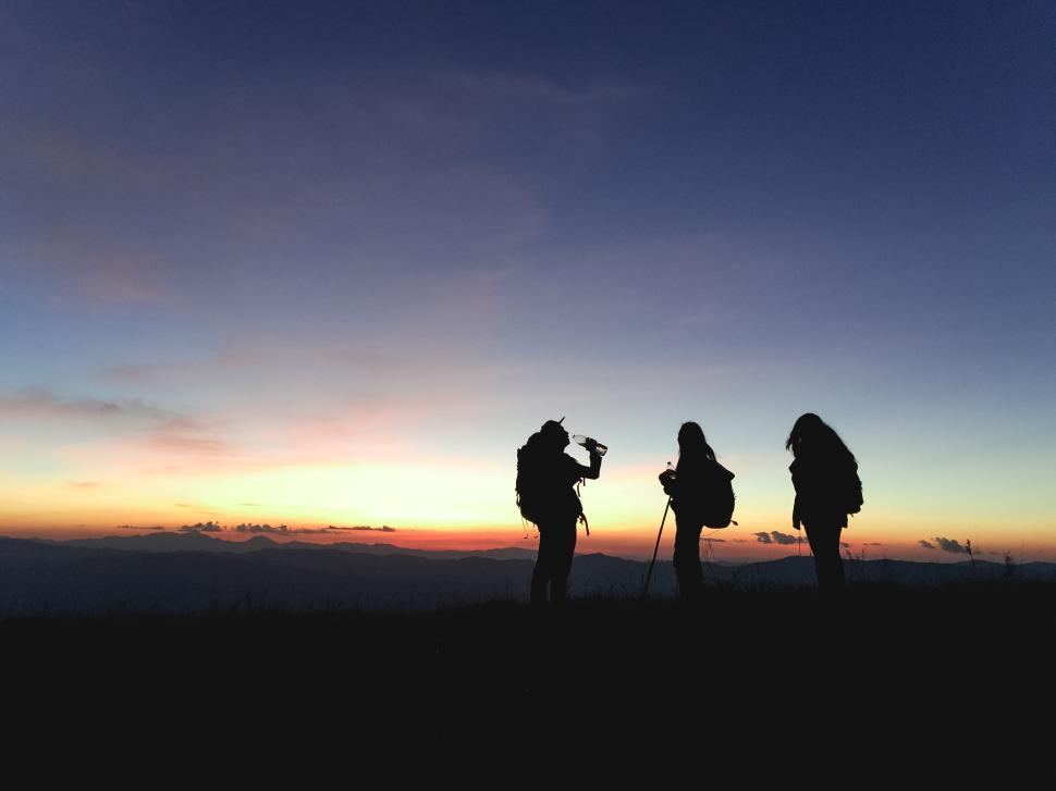 Free Image of Three hikers with equipment silhouetted by sunset sky. 