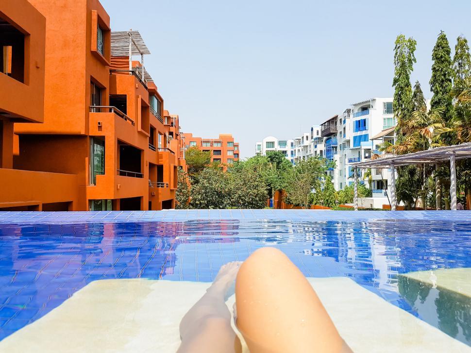 Free Image of Person relaxing in a pool with modern apartments nearby. 