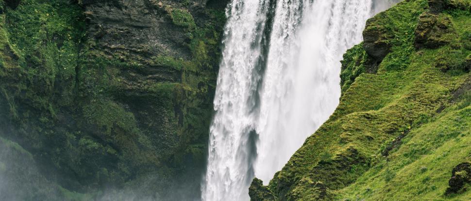 Free Image of Stunning waterfall flowing through lush green rocky cliffs 